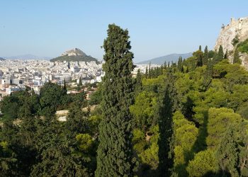 View of Athens on a sunny day with a clear sky showing Lycabettus Hill, the Acropolis rock and the dense greenery of Filopappou hill in the foreground