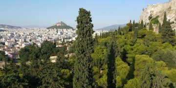 View of Athens on a sunny day with a clear sky showing Lycabettus Hill, the Acropolis rock and the dense greenery of Filopappou hill in the foreground