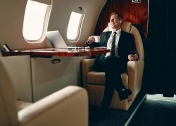 Businessman in private jet Senior businessman in suit flying in private jet and listening to music via wireless earphones.