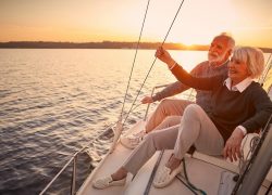 Enjoying luxury life. Beautiful happy senior couple in love relaxing on the side of sailboat or yacht deck floating in sea at sunset, looking at amazing evening view. Vacation, travelling, boat tour