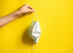 Medical,Mask,In,A,Girl's,Hand.,Yellow,Background.